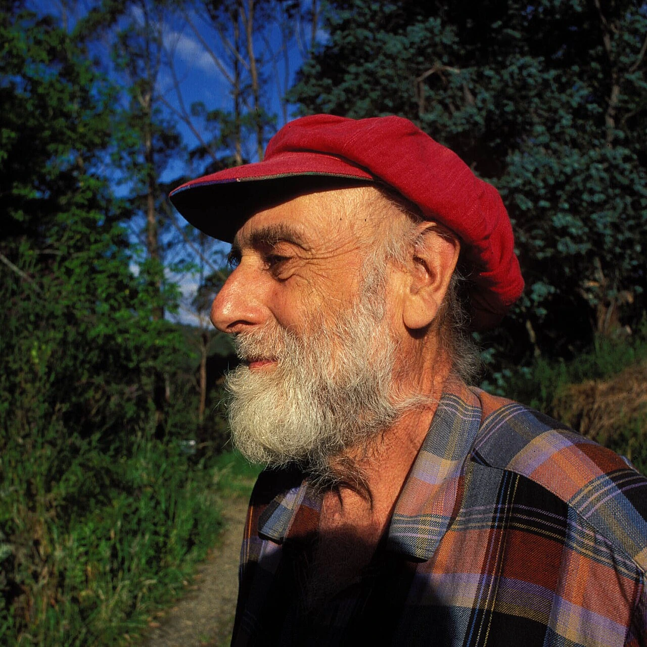 Portrait couleur de Friedensreich Hundertwasser de profil, portant une casquette rouge et une chemise à carreaux, en ext